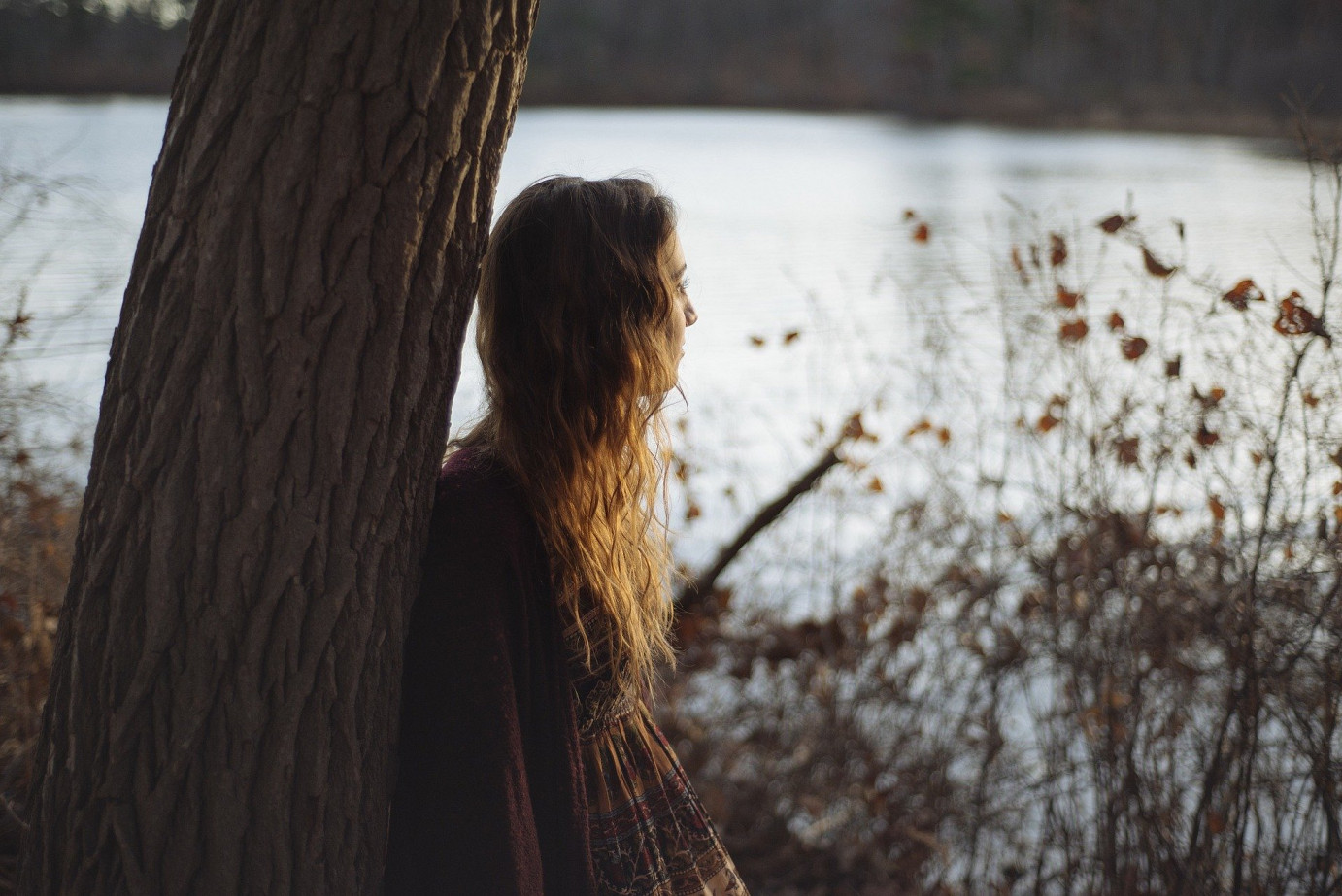 Ein Mädchen angelehnt an einen Baum und den Blick auf einen See gerichtet