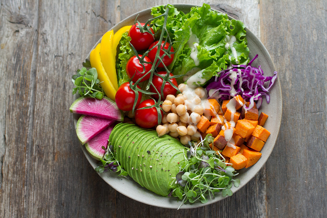 Ein Teller angerichtet mit Avocado, Süßkartoffeln, Kicherersen, Tomate, Salat, Paprika, Rotkraut