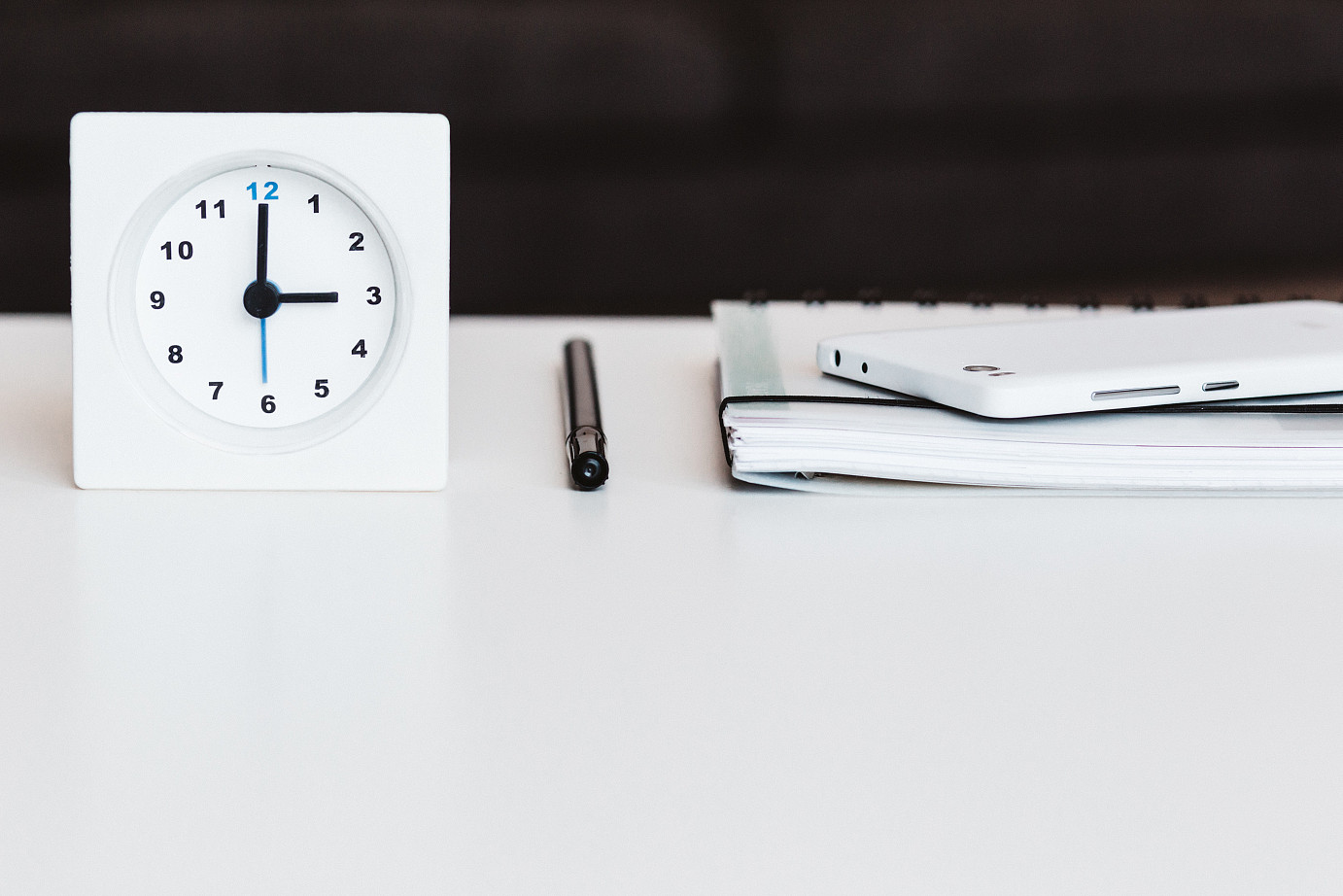 Uhr, Stidt, Kalender und Handy auf einem weißen Tisch vor einem schwrzen Hintergrund.